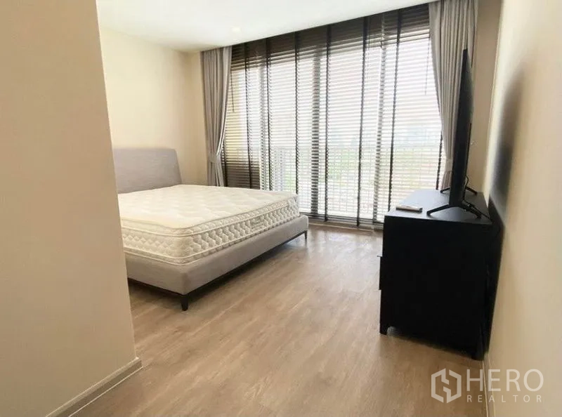 Condominium for rent in Pathum Wan, Bangkok - Primary bedroom with large window wall, curtains, and bed facing a TV cabinet.