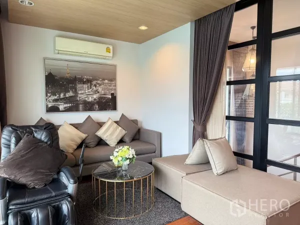 Detached House for rent or sale in Prawet, Bangkok - Cozy lounge with sectional sofa, recliner and floor-to-ceiling windows beside a glass partition.