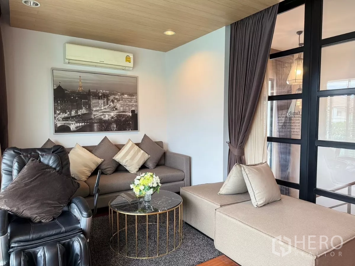 Detached House for rent or sale in Prawet, Bangkok - Cozy lounge with sectional sofa, recliner and floor-to-ceiling windows beside a glass partition.