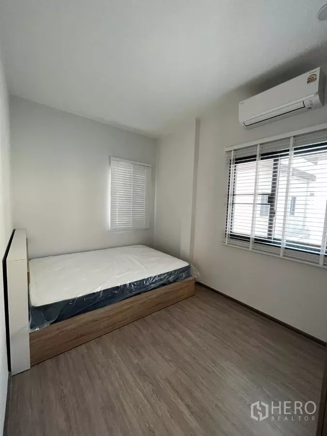 Detached House for rent or sale in Bang Phli, Samut Prakan - Secondary bedroom with a bed, wood-style flooring, and two bright windows.