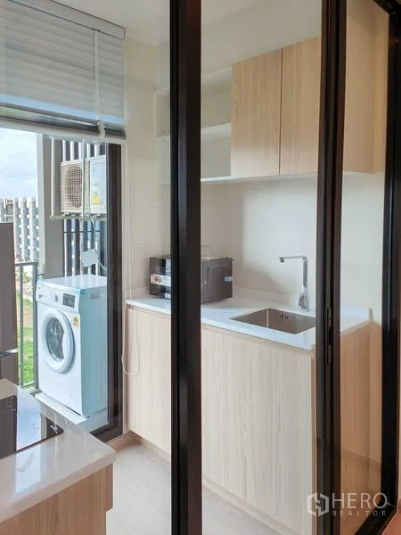 Condominium for rent - Separate kitchen with light-wood cabinets, sink and balcony laundry zone with washing machine.