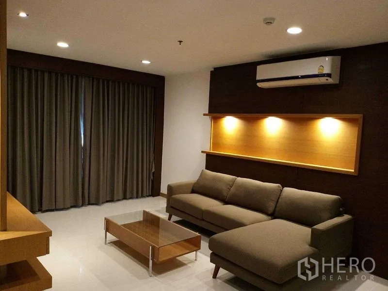 Condominium for rent in Sathon, Bangkok - Cozy lounge featuring a grey sofa, illuminated wall niche, coffee table, and blackout curtains.