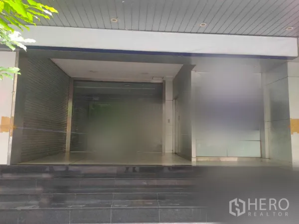 办公空间 出租在Yan Nawa, Bangkok - 曼谷办公楼入口，玻璃门立面，带遮雨棚与深色台阶，旁设卷闸空间。