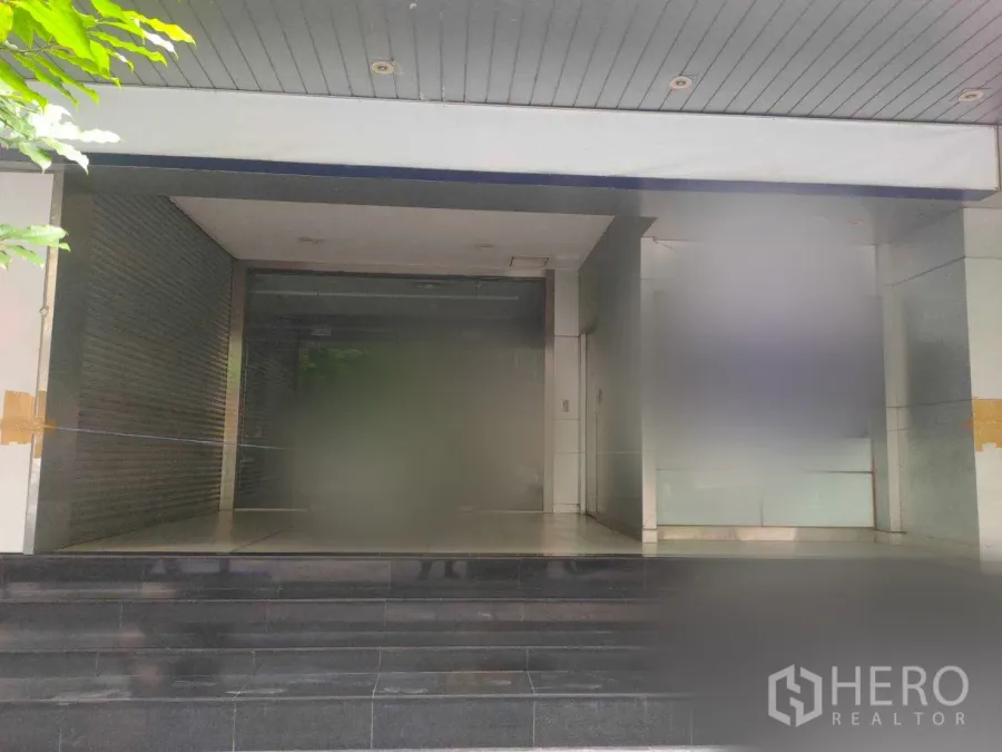 办公空间 出租在Yan Nawa, Bangkok - 曼谷办公楼入口，玻璃门立面，带遮雨棚与深色台阶，旁设卷闸空间。