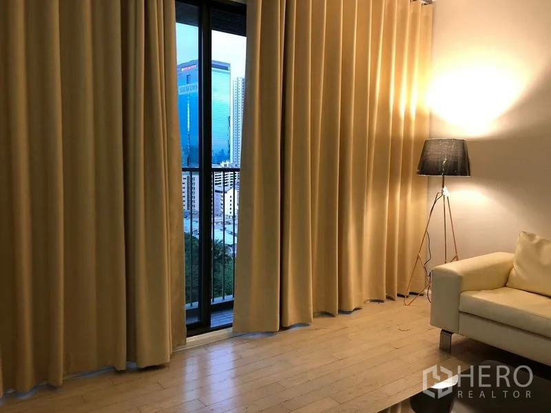 คอนโด ขายในWatthana, Bangkok - ประตูกระจกสไลด์ออกสู่ระเบียงหลังผ้าม่านยาว เห็นวิวเมือง โคมไฟยืนและโซฟา