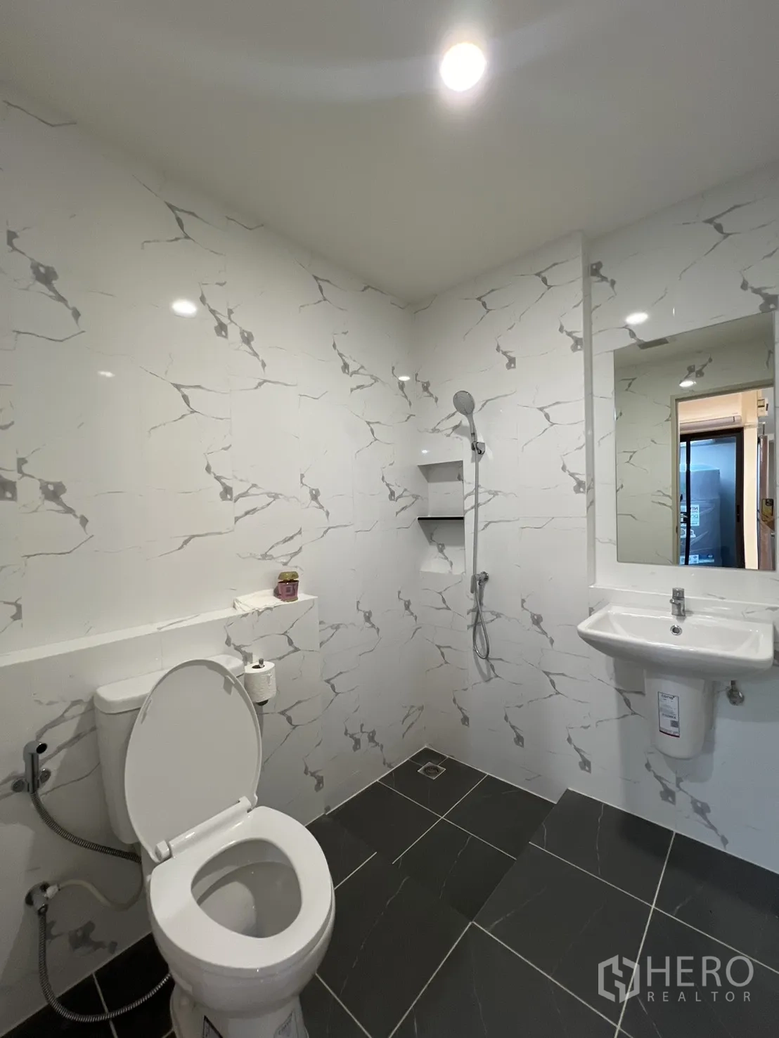 Townhouse for rent in Bang Phli, Samut Prakan - Modern bathroom with marble-pattern tiles, toilet, sink, mirror and a handheld shower.