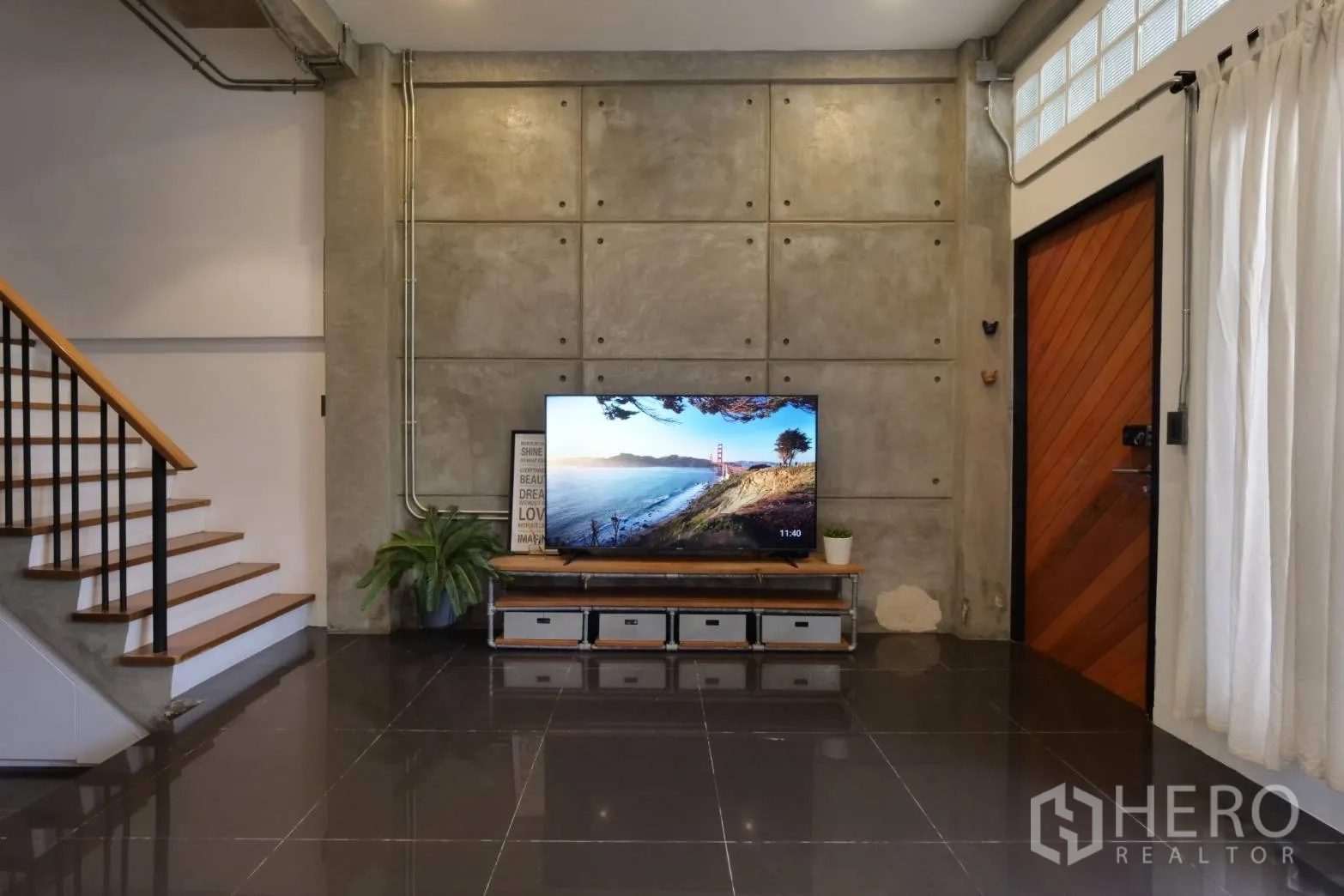 Townhouse for rent in Khlong Toei, Bangkok - TV feature wall with exposed concrete panels and low media unit.