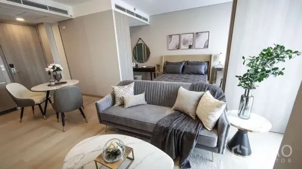 Condominium for sale in Khlong Toei, Bangkok - Open-plan Siamese Exclusive Queens condo with grey sofa, marble coffee table, dining set, and bed by a large window.