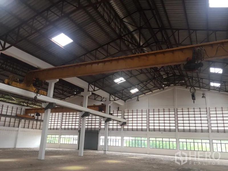 Warehouse for rent in Lam Luk Ka, Pathum Thani - Overhead gantry crane beneath a high roof inside the warehouse, with wide entry door and surrounding windows.
