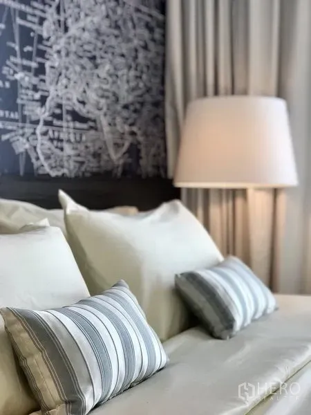 คอนโด ให้เช่าในKhlong Toei, Bangkok - ภาพระยะใกล้ของเตียงปูผ้าขาว หมอนลายทาง และโคมไฟข้างเตียง หน้าผนังลายแผนที่