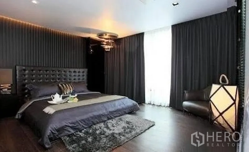 Townhouse for rent in Watthana, Bangkok - Spacious master bedroom with dark curtains, tufted headboard and rug.