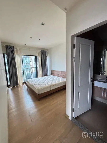 คอนโด ให้เช่าในBangkok - ห้องนอนหลักพร้อมหน้าต่างบานใหญ่ พื้นไม้ และประตูเข้าสู่ห้องน้ำในตัว