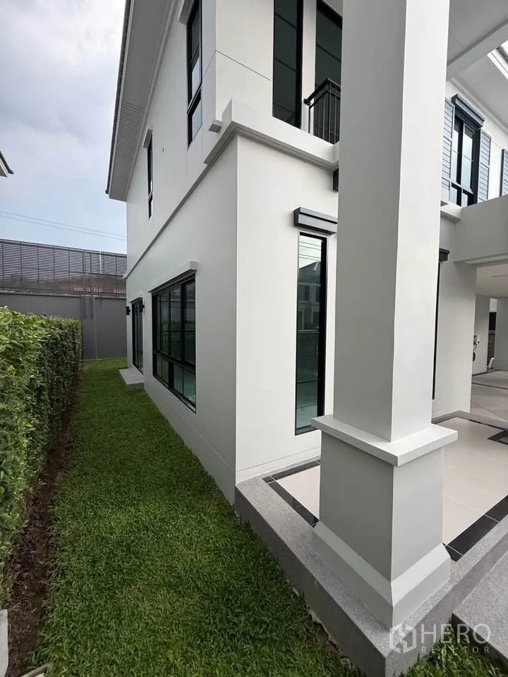 Detached House for rent in Don Mueang, Bangkok - Side yard with lawn beside the white two-storey house.