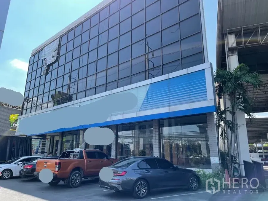 货栈 出租在Prawet, Bangkok - 玻璃幕墙商业建筑外立面，前方设停车位。