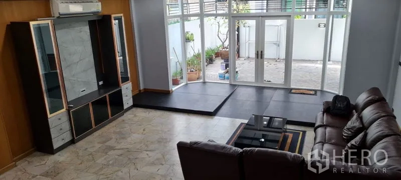 Townhouse for rent in Watthana, Bangkok - Bright lounge opening to a private patio through full-height glass doors, with display cabinet and sofa.