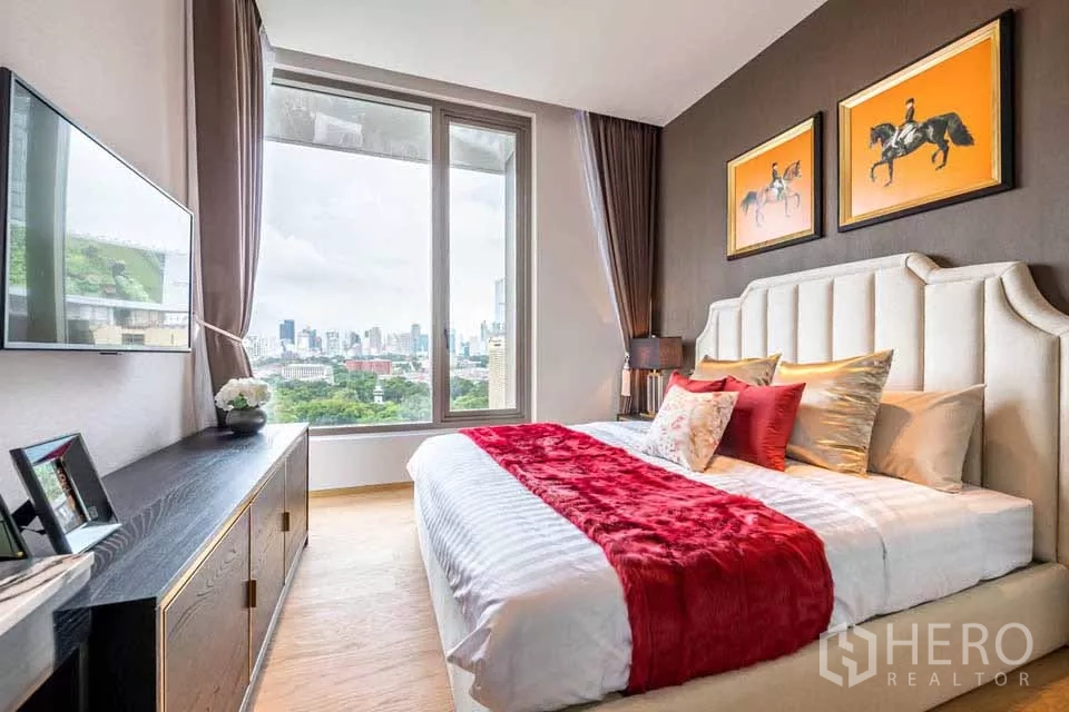 公寓 出租或出售在Bang Rak, Bangkok - 卧室配大窗，公园与城市景观，墙挂电视与红色毯毯点缀。