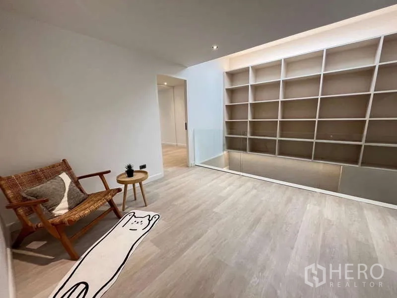Townhouse for sale in Khlong Toei, Bangkok - Bright upstairs landing with built-in shelving wall, wicker chair and light wood flooring.