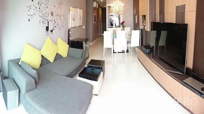 Condominium for rent or sale in Watthana, Bangkok - Open-plan living and dining room with sectional sofa, large TV and custom media cabinetry.