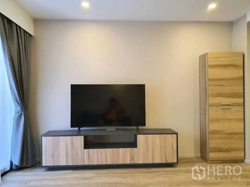 Condominium for rent in Sathon, Bangkok - Bright living room with flat-screen TV on a wood console and floor-to-ceiling curtains.