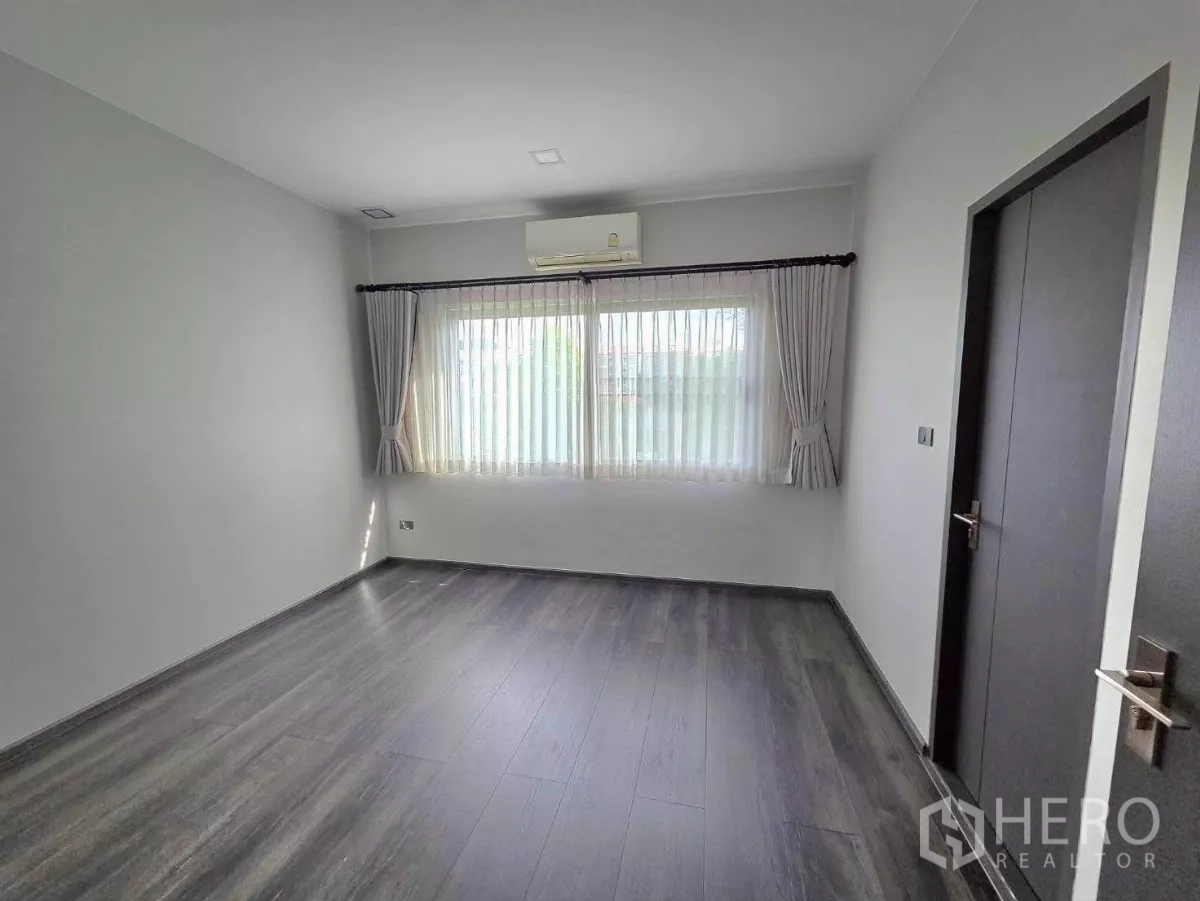 Detached House for rent in Bang Phli, Samut Prakan - Third bedroom with wood-look floors, air-conditioner and a wide window with sheer curtains.