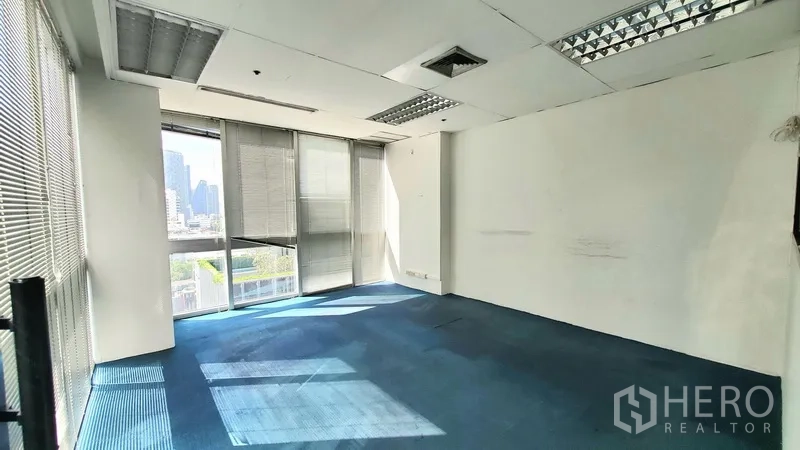 Office Space for rent in Khlong Toei, Bangkok - Private office with large windows, blinds, blue carpet, and city view near BTS Thong Lo.
