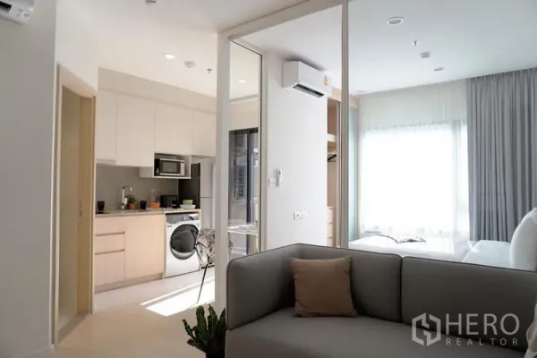 公寓 出租在Pathum Wan, Bangkok - 内置橱柜的小厨房与洗衣机，旁边是通往明亮卧室的玻璃滑门