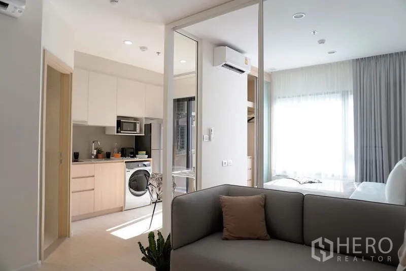 公寓 出租在Pathum Wan, Bangkok - 内置橱柜的小厨房与洗衣机，旁边是通往明亮卧室的玻璃滑门