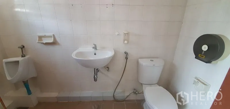 Home Office for rent in Khlong Toei, Bangkok - White tiled restroom with toilet, urinal and wall-mounted sink.