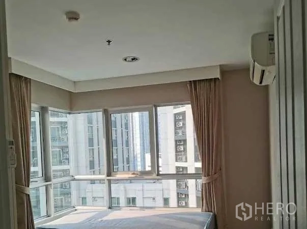 Condominium for rent in Huai Khwang, Bangkok - Corner bedroom with wraparound windows, city view, beige curtains and a wall-mounted air conditioner.