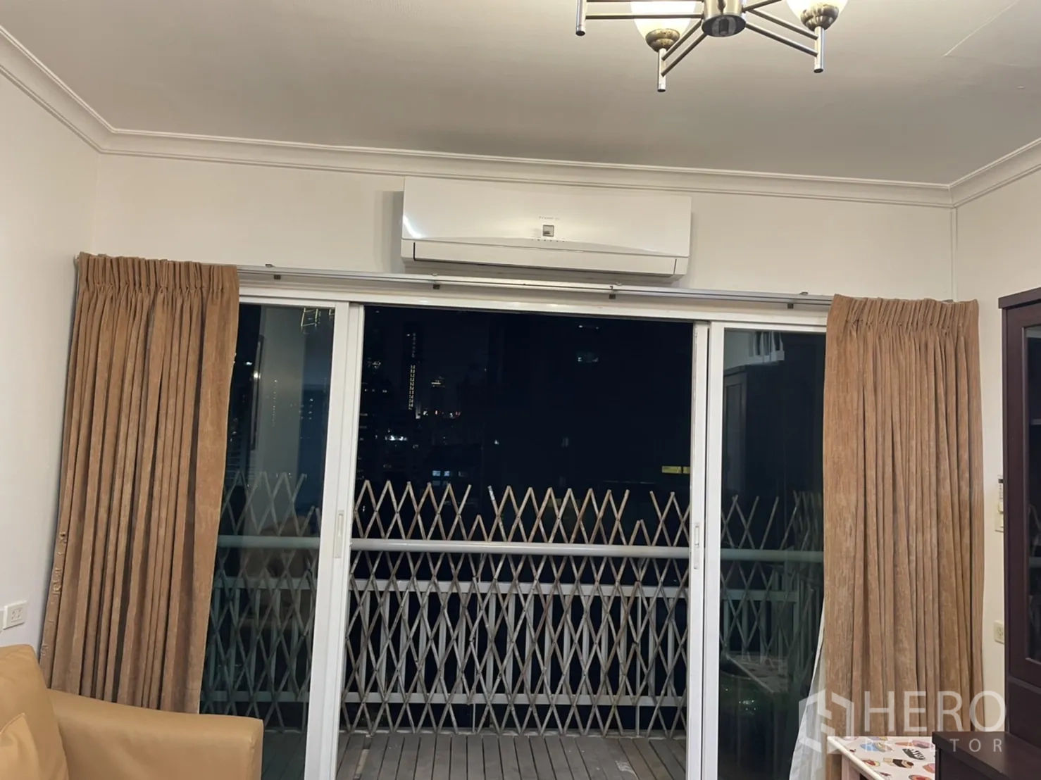 公寓 出租在Watthana, Bangkok - 客厅推拉玻璃门通向阳台，配窗帘与空调，可见城市夜景。