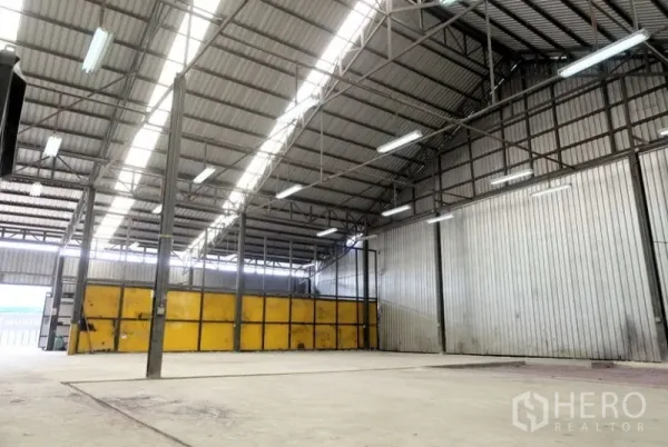 Warehouse for rent in Pak Kret, Nonthaburi - Wide warehouse bay with a high gabled roof and fluorescent lighting.