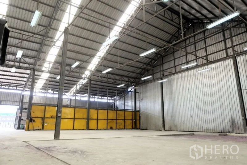 Warehouse for rent in Pak Kret, Nonthaburi - Wide warehouse bay with a high gabled roof and fluorescent lighting.