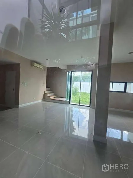 Detached House for rent in Bueng Kum, Bangkok - Bright open-plan living area with glossy tile floors, sliding glass doors to a lawn, and a staircase.