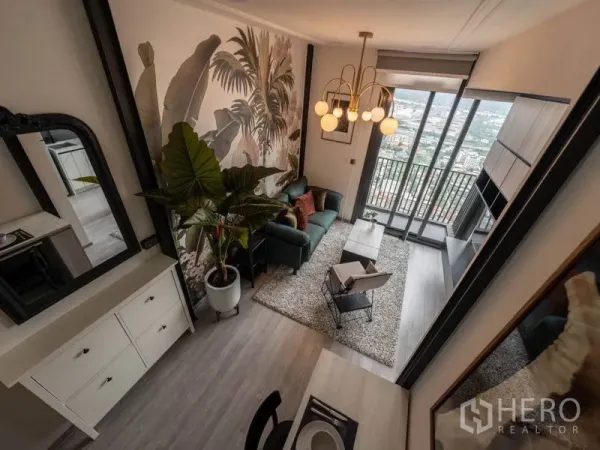 公寓 出租或出售在Phra Khanong, Bangkok - 客厅带热带风壁画与吊灯，绿色沙发，落地窗连接阳台可观城市景色。