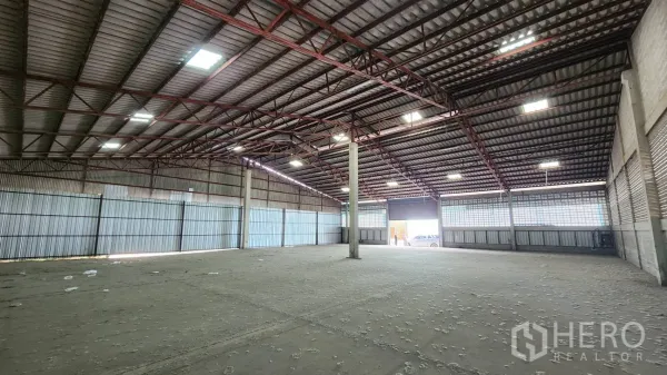 Warehouse for rent in Krathum Baen, Samut Sakhon - Open-plan storage hall showing roller shutters, a central column, and parking visible outside.