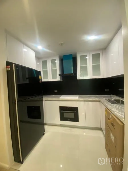 อพาร์ทเมนท์ ให้เช่าในWatthana, Bangkok - ครัวรูปตัว L โทนขาวเงา แผงกันเปื้อนสีดำ เตาอบบิวท์อิน และตู้เย็นขนาดใหญ่