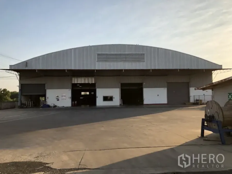 Factory for rent in Bang Pakong, Chachoengsao - Large steel-arch factory exterior with multiple roller shutter doors and a wide concrete truck yard in Bang Pakong, Chachoengsao.