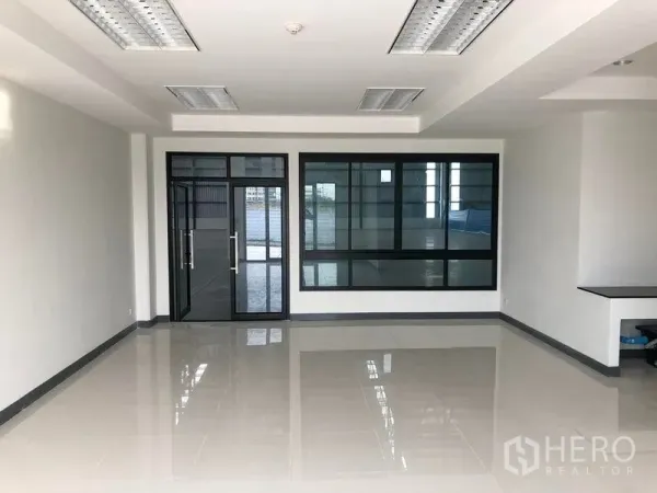 Factory for rent in Samut Prakan - Bright tiled office interior with glass doors and black‑framed windows overlooking the warehouse.