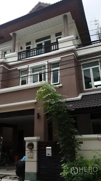 Detached House for rent in Wang Thonglang, Bangkok - Three-storey detached house exterior with brown and white facade, balcony, gated carport and climbing greenery.