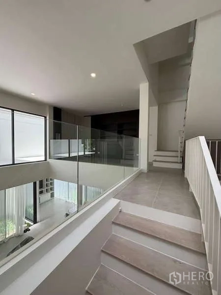 Townhouse for rent or sale in Don Mueang, Bangkok - Upper mezzanine hall with glass balustrade overlooking the living area below.