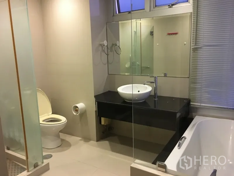 Condominium for rent in Khlong Toei, Bangkok - Contemporary bathroom featuring glass shower, bathtub, vessel sink, and wide mirror.