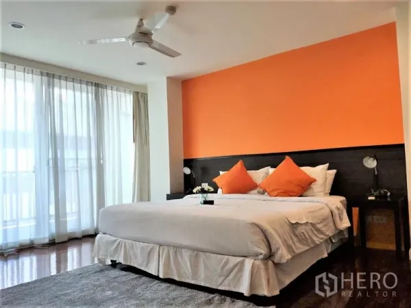 Condominium for rent in Bang Rak, Bangkok - Guest bedroom with orange feature wall, large bed, ceiling fan and full-height balcony windows.