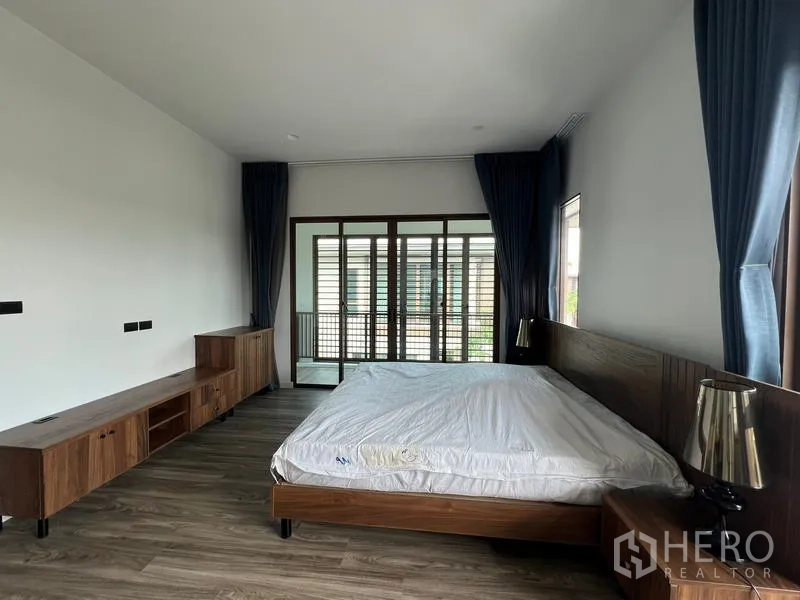 Detached House for rent in Bang Kapi, Bangkok - Spacious master bedroom with wood furniture, large windows and sliding doors to a balcony.