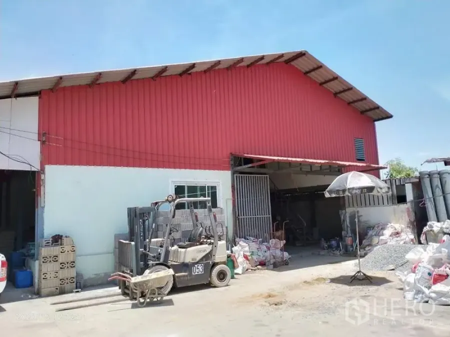 Warehouse for rent or sale in Lam Luk Ka, Pathum Thani - Red metal-clad warehouse with a high gable roof and sliding gate, with a loading area in front.