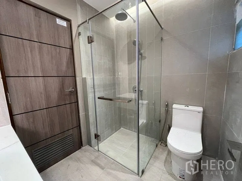 联排别墅 for rent in Phra Khanong, Bangkok - 浴室配玻璃淋浴间与马桶，灰色中性色调。