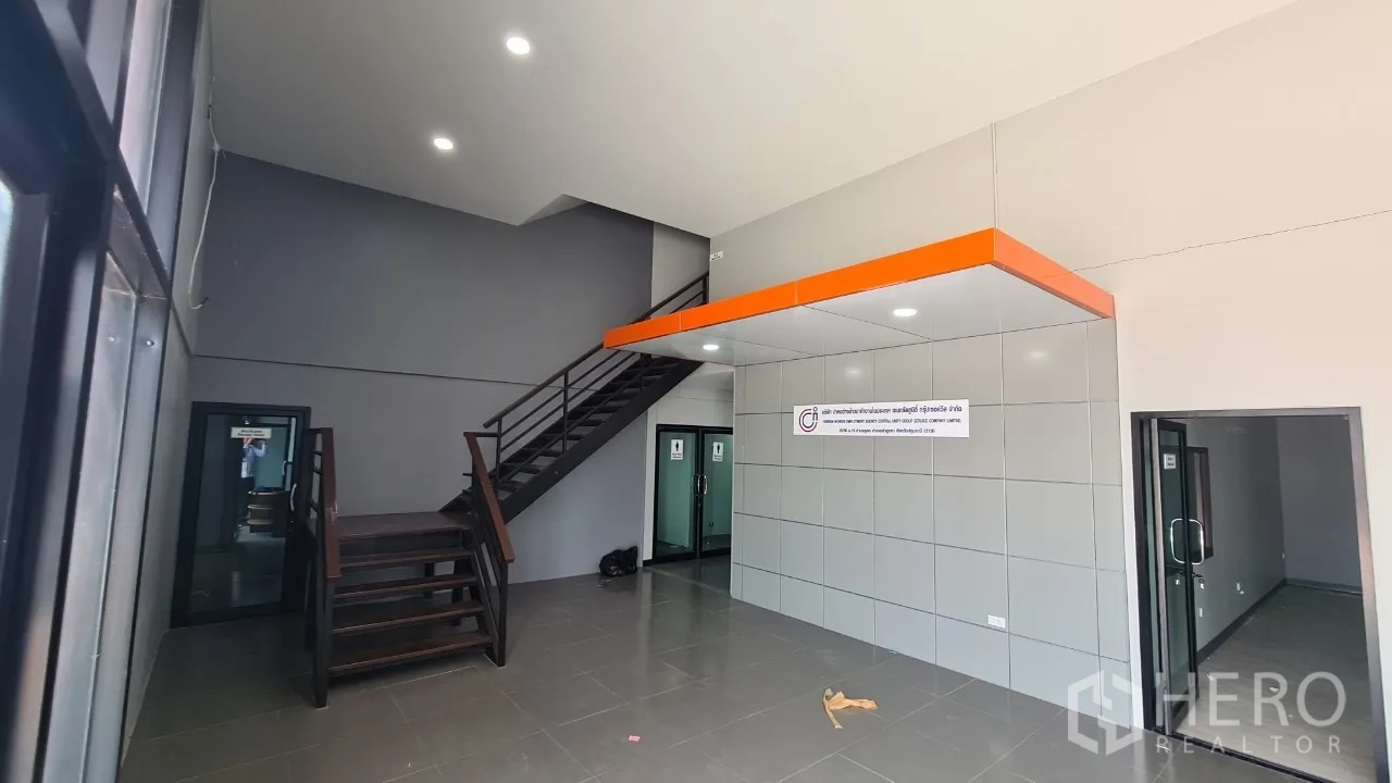 Home Office for rent in Pathum Thani - Double-height reception hall with steel staircase, orange feature soffit and glass doors.