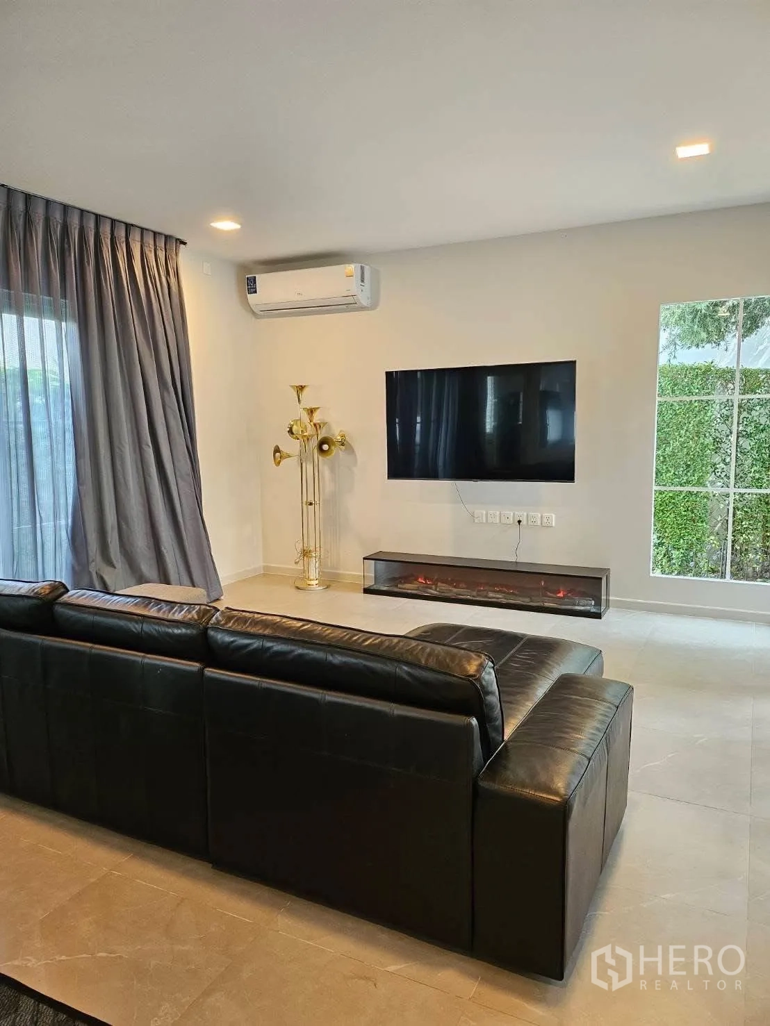 บ้านเดี่ยว for rent in Bang Phli, Samut Prakan - ห้องนั่งเล่นมีโซฟาหนังสีดำ ทีวีติดผนัง เครื่องปรับอากาศ และดีไซน์เตาผิงยาว