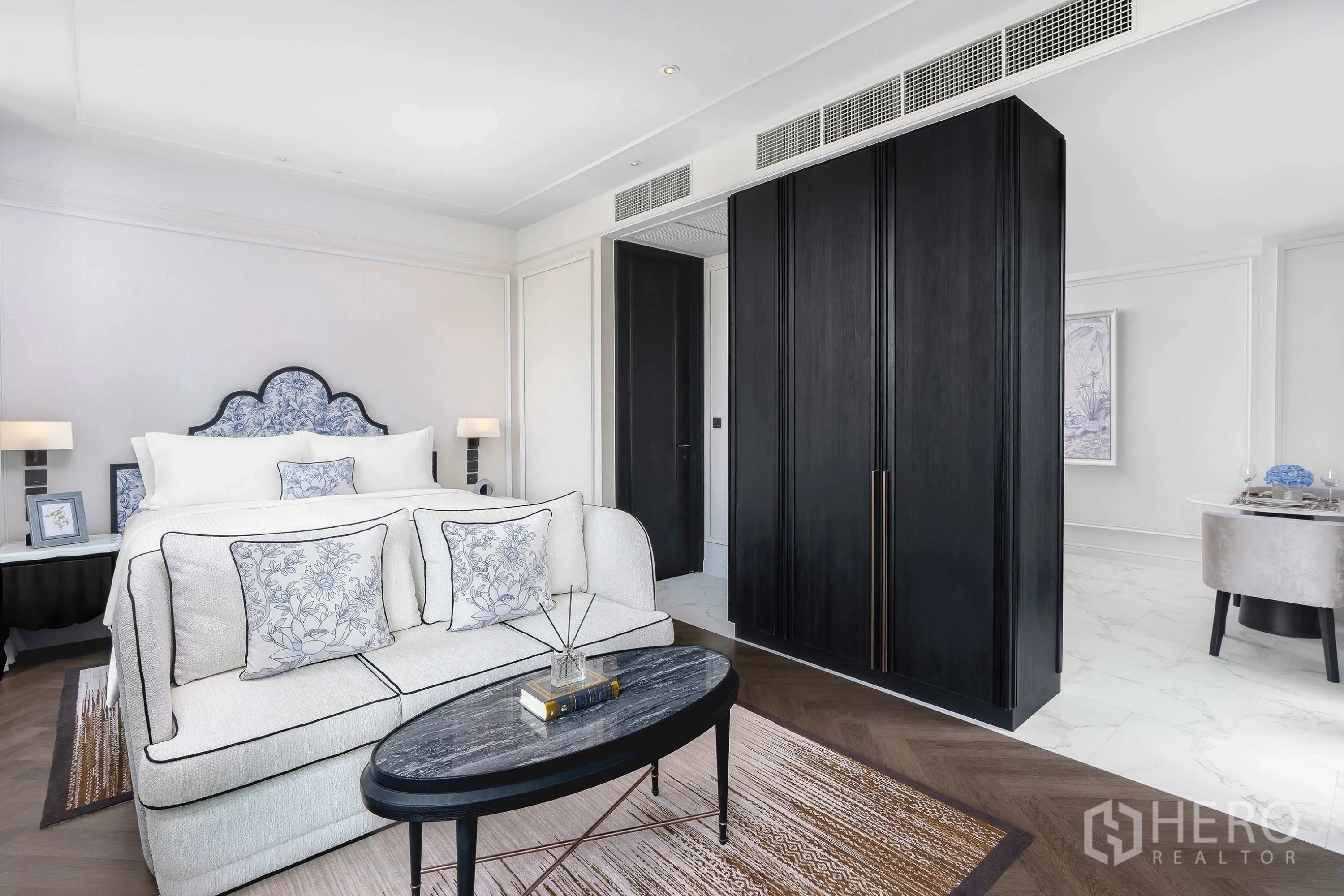 Condominium for rent in Khlong Toei, Bangkok - Cozy sofa and coffee table at the foot of the bed with tall wardrobe and herringbone floor.
