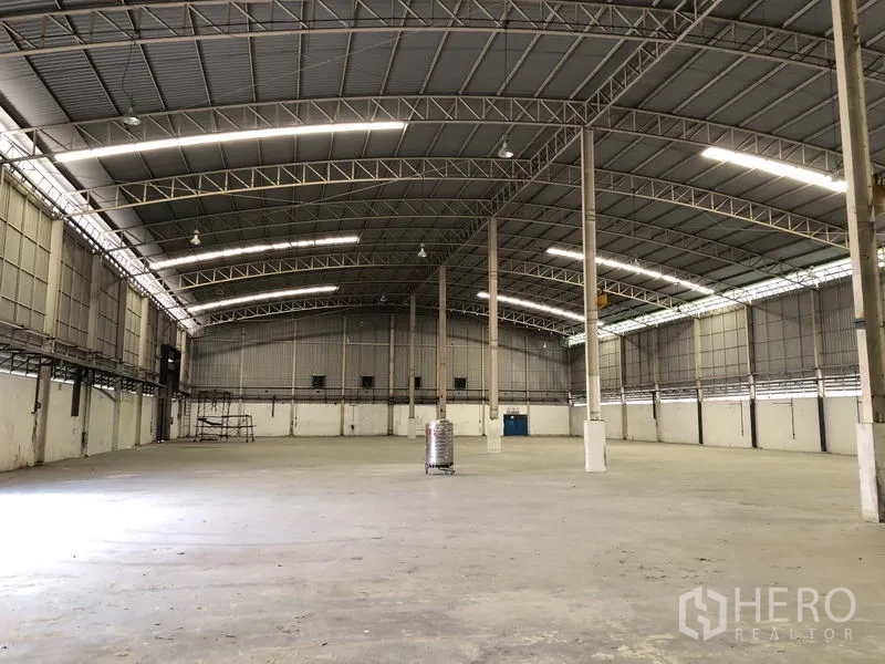 工厂 出租在Phra Nakhon Si Ayutthaya - 空旷仓库内部，拱形钢结构屋顶、混凝土地面与采光板。