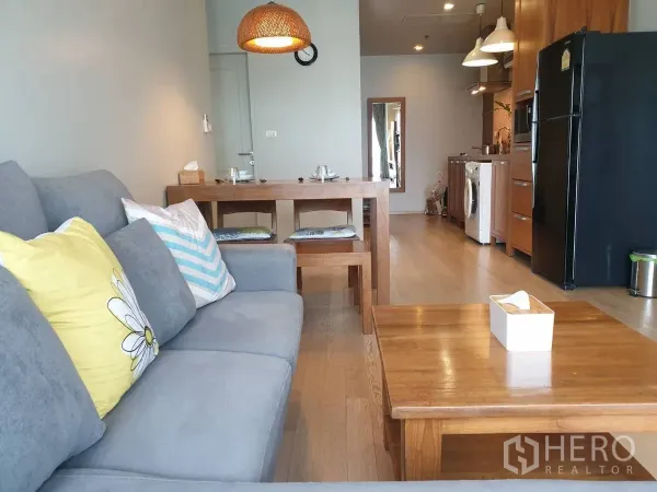 คอนโด ให้เช่าหรือขายในBangkok - โซฟาสีเทาและชุดทานอาหารหันหน้าไปยังครัวคอมแพคในพื้นที่เปิด